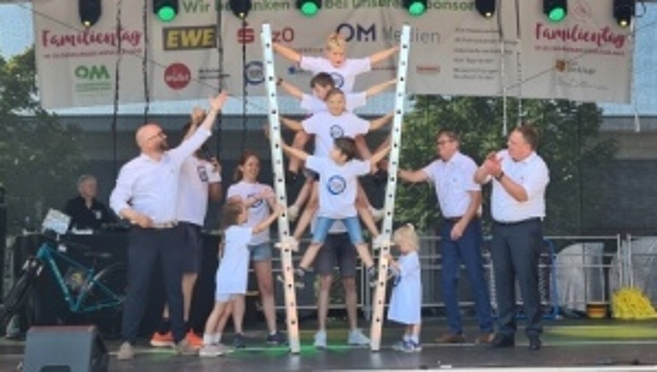 Kinder bauen eine Pyramide mit Leitern auf einer Bühne, mit dabei zwei Landräte und der Bürgermeister