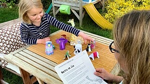 Mädchen spielt mit Zoo-Tieren und eine Frau hält ein Blatt in der Hand