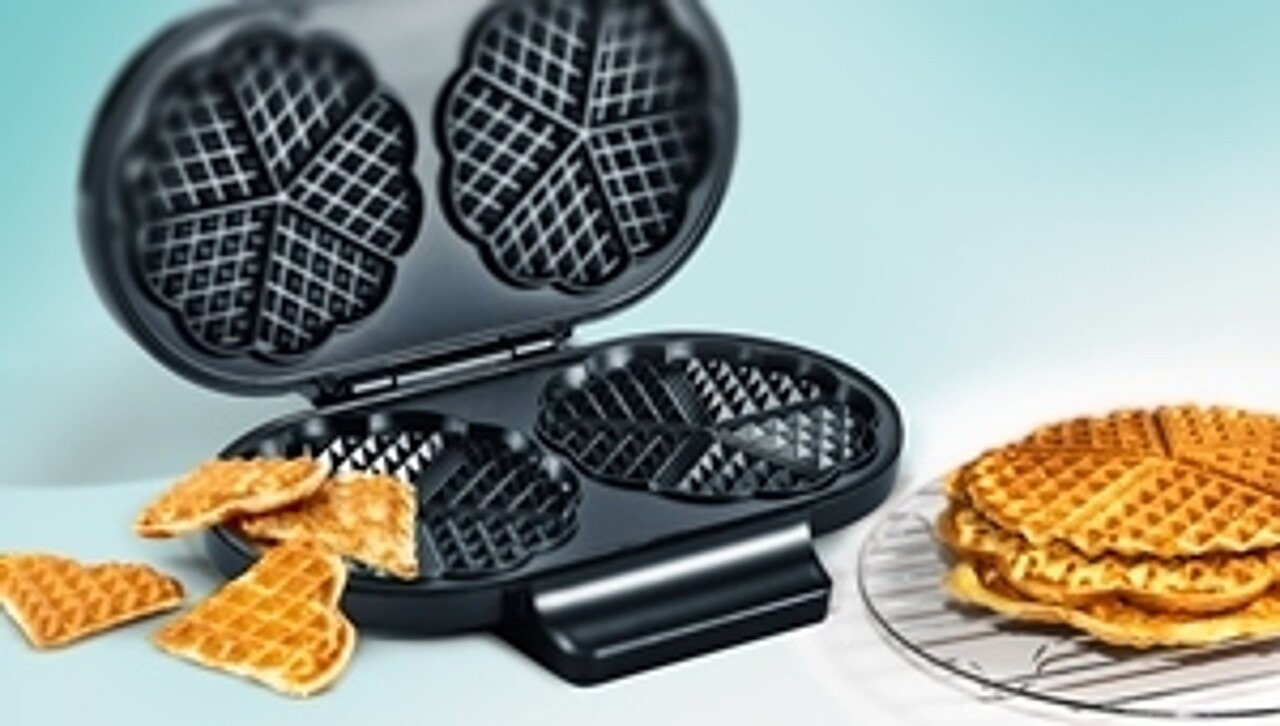 Doppel-Waffeleisen in klassischer Herzform mit frisch gebackenen Waffeln daneben.