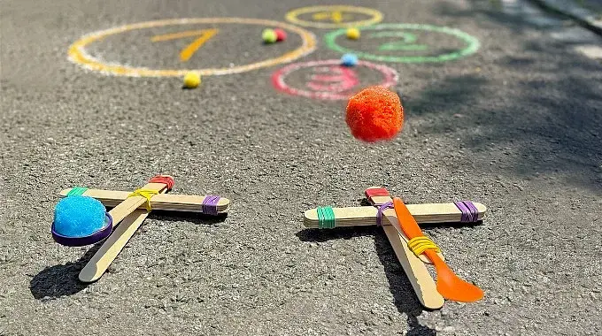 © Ina Kerckhoff Zwei selbstgebaute Katapulte aus Holzstäbchen und Haushaltsgummis: Von einem fliegt ein Schwämmchen durch die Luft Richtung Kreide-Kreise auf der Straße.