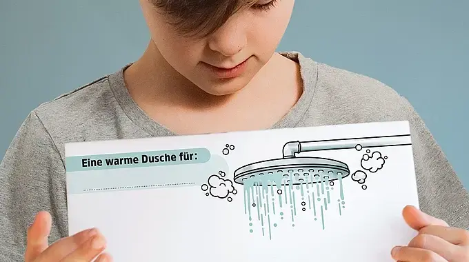 © Illustration Ina Kerckhoff Ein Junge zeigt die PDF-Vorlage für die Warme Dusche mit einem Bild von einem Duschkopf, darunter viel Platz für positive Botschaften.