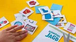 © KiKA Kinderhände halten und schneiden bunte Motivkarten aus der Bastelvorlage aus.