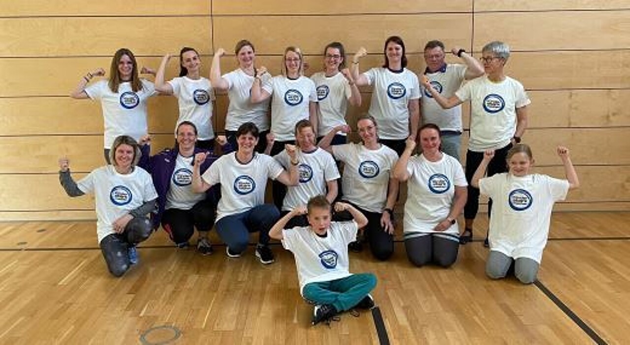 Die Schulungs-Teilnehmerinnen und Teilnehmer im „Kinder stark machen"-T-Shirt markieren Stärke, in dem sie eine Faust machen.