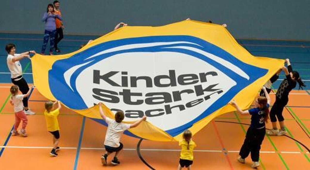 Viele Kinder gemeinsam spannen das Rundbanner mit der Aufschrift „Kinder stark machen“.