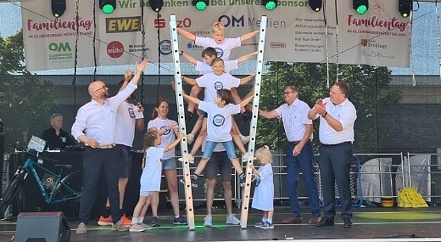 Kinder bauen eine Pyramide mit Leitern auf einer Bühne, mit dabei zwei Landräte und der Bürgermeister