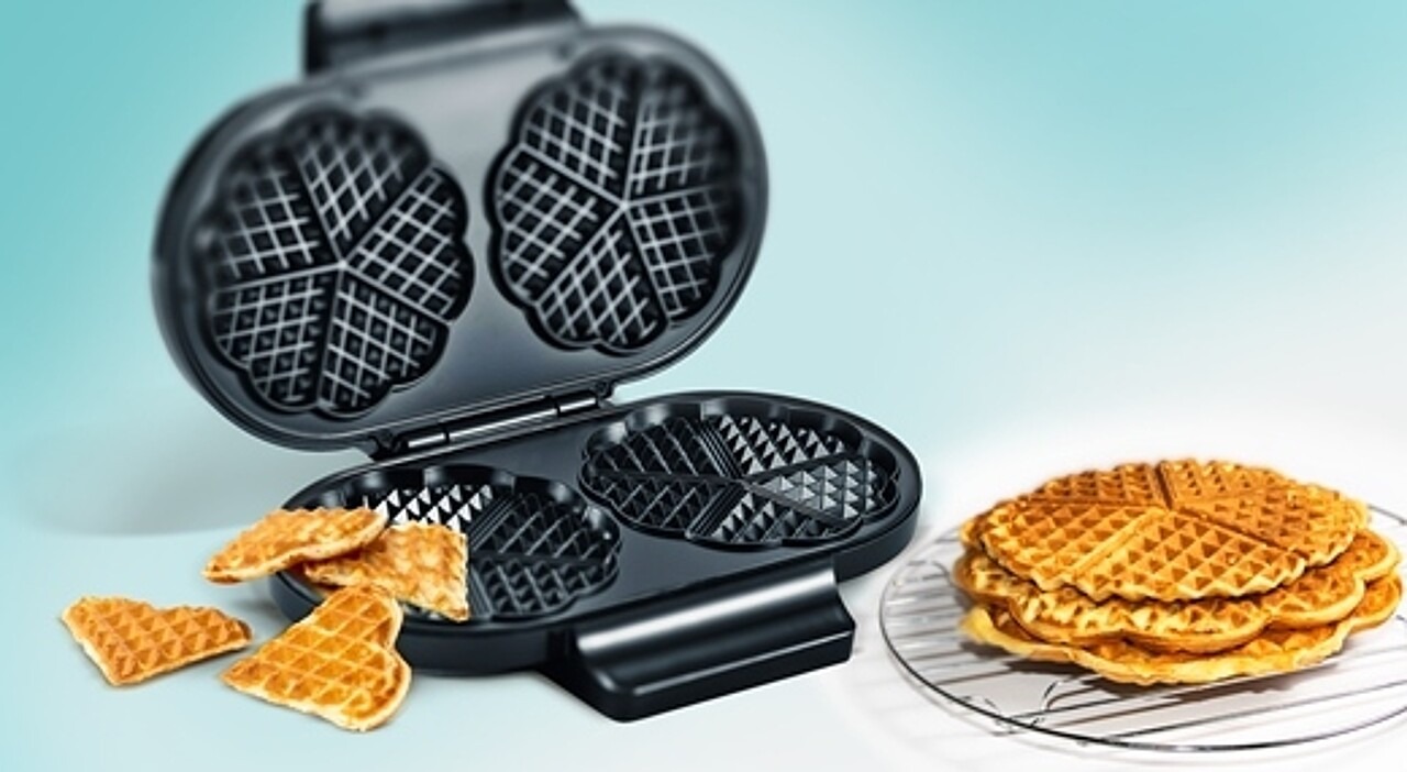 Doppel-Waffeleisen in klassischer Herzform mit frisch gebackenen Waffeln daneben.