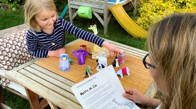 Mädchen spielt mit Zoo-Tieren und eine Frau hält ein Blatt in der Hand